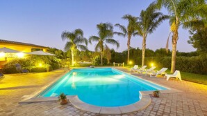 A swimming pool with lounge chairs and palm trees.