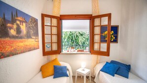 A room with two beds, a small table, a window with curtains, and a painting on the wall.