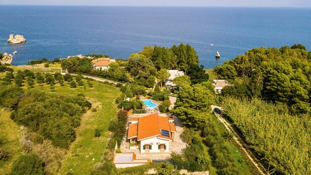 A coastal property with a swimming pool, surrounded by lush greenery and a clear view of the sea.