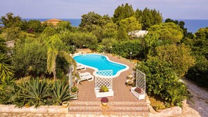 A pool surrounded by lush greenery and a view of the sea.