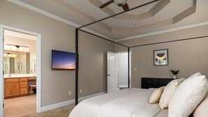 A bedroom with a bed, a TV, a ceiling fan, a door, and a bathroom visible through an open door.