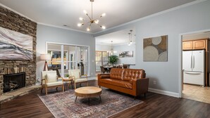 A spacious living room with a stone fireplace, leather sofa, and a dining area in the background.