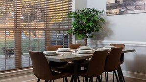 A dining area with a table set for six, a potted plant, and a modern chandelier.