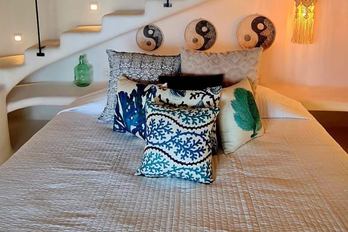 Un dormitorio con una cama, almohadones decorativos, una lámpara colgante y una escalera.