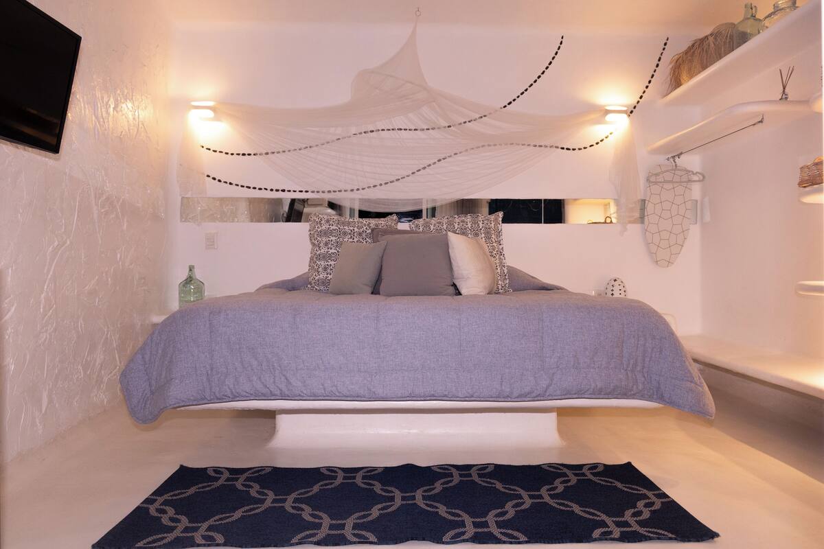 Un dormitorio con cama, mesitas de noche, una mosquitera colgante y una alfombra estampada.