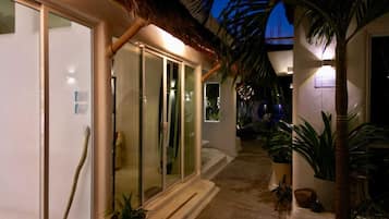 A corridor with glass doors, potted plants, and a thatched roof structure.