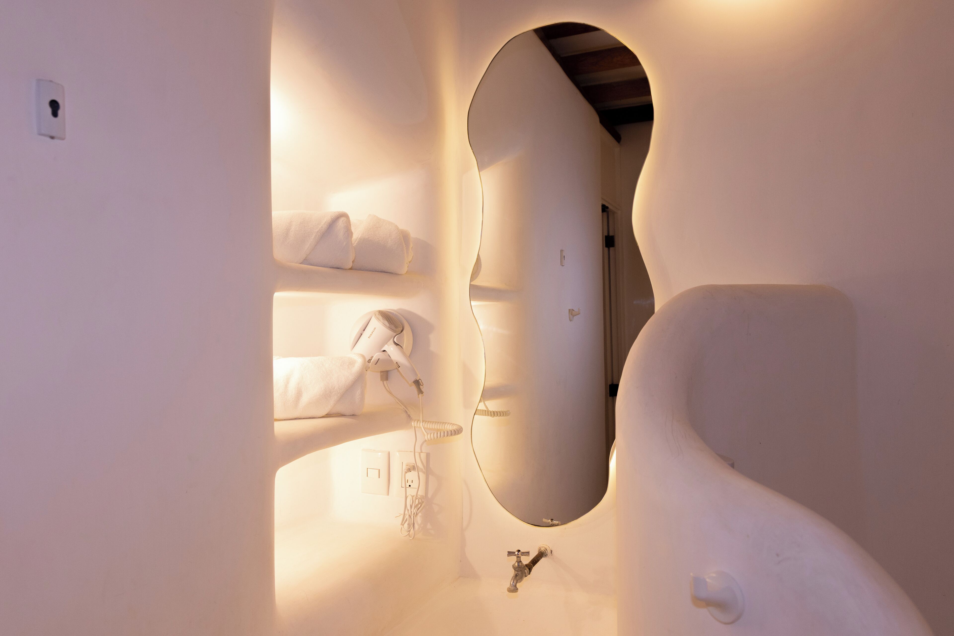 A bathroom with a unique curved mirror, a towel rack, and a sink.
