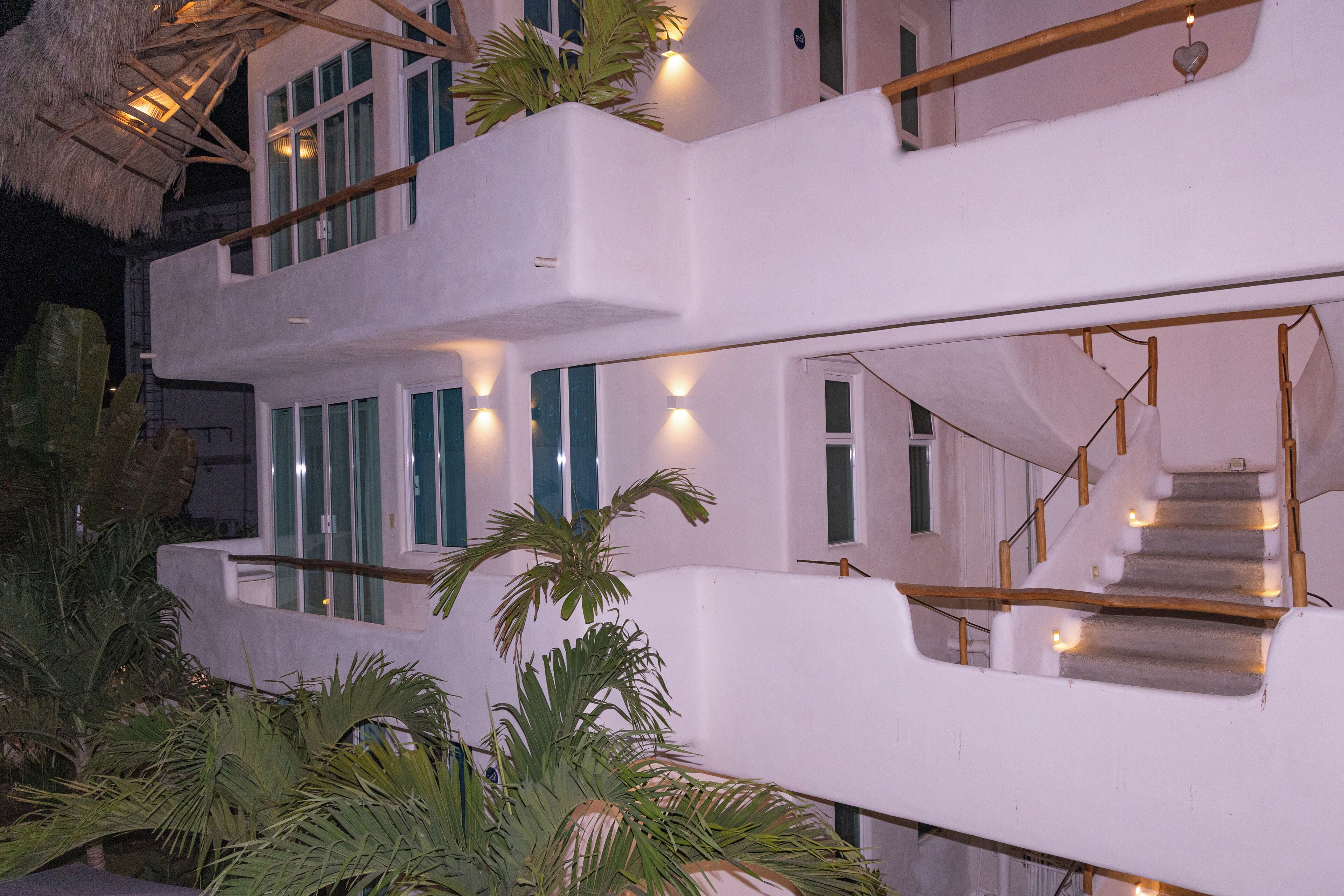 Un immeuble à plusieurs étages, à la façade blanche, doté de grandes fenêtres et d’un escalier avec des rampes en bois.