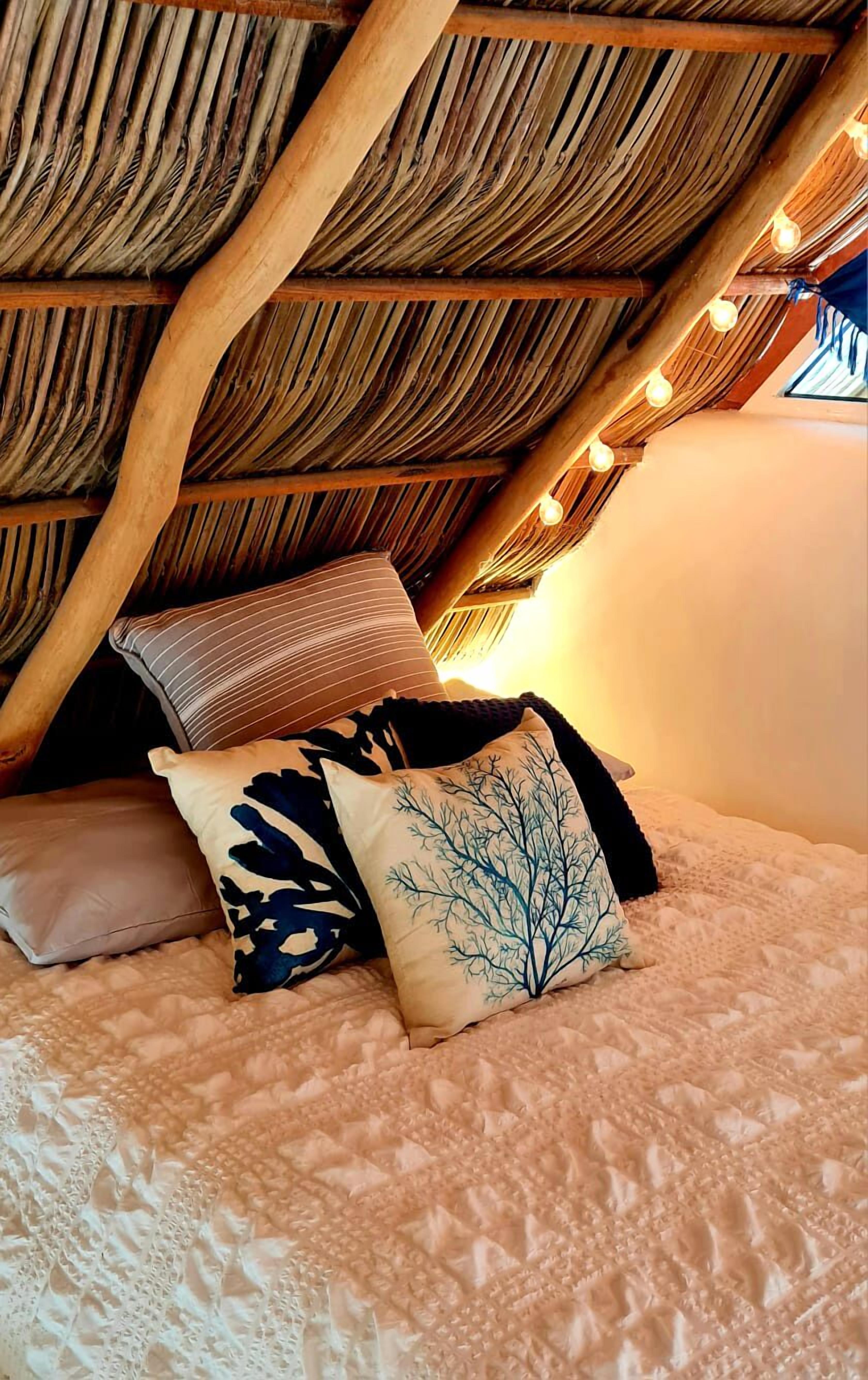 A cozy attic bedroom with a sloped ceiling, string lights, and a bed with patterned pillows.
