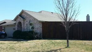 A residential house with a stone facade, a wooden deck, and a single tree in the yard.