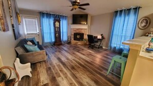 A living room with a fireplace, a sofa, a dining table, and a ceiling fan.