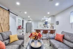 A modern living room with grey sofas, a coffee table with a vase of flowers, and a kitchen in the background.