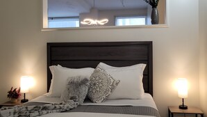 Un dormitorio ordenado con una cama grande, dos lámparas de noche, una lámpara decorativa en el techo y un ventanal con vistas.