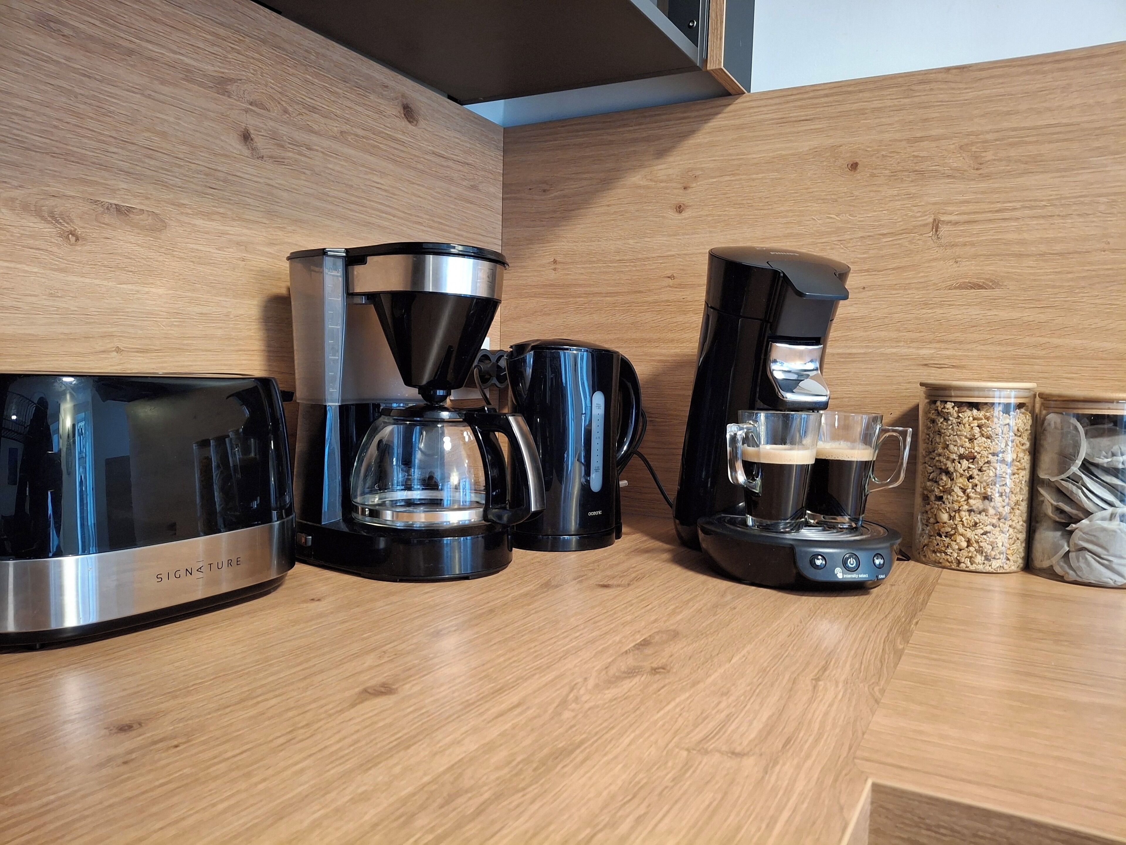 Een keuken met een koffiezetapparaat, een koffiekan en een pot koffiebonen op het aanrecht.
