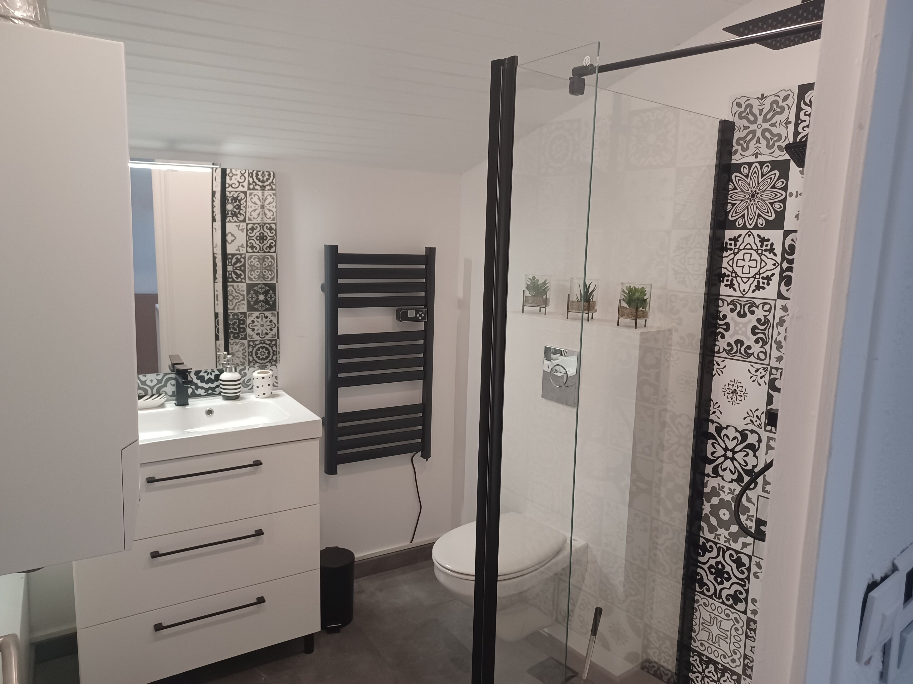 Une salle de bain moderne avec un lavabo blanc, un porte-serviettes noir et des carreaux à motifs.