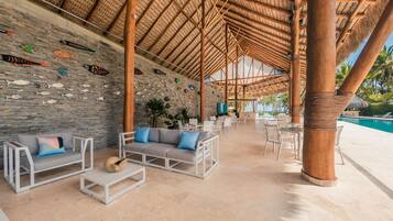 An outdoor lounge area with a stone wall, wooden furniture, and a pool.