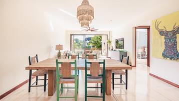 A spacious dining area with a large wooden table and green chairs, a chandelier, and a view of the outdoors.
