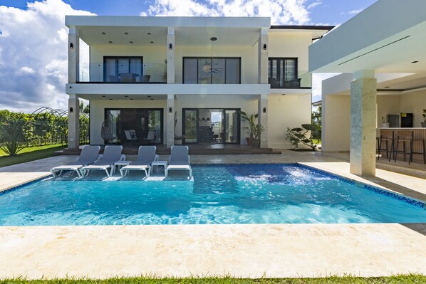 Ein modernes, zweistöckiges Haus mit Swimmingpool, Sitzgelegenheiten im Freien und einer Terrassenanlage.