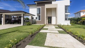 A modern two-story house with a covered driveway, a well-maintained lawn, and a stone pathway leading to the entrance. - Brand new luxury villa located in a the most pristine gated community SOV
 (Sosúa)