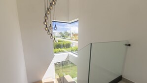 A modern staircase with glass railings and a view of a green landscape through a large window. - Brand new luxury villa located in a the most pristine gated community SOV
 (Sosúa)