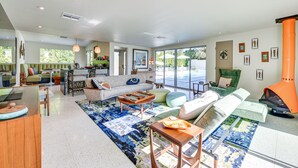 A spacious living area with a sofa, coffee table, and a dining table. There are multiple chairs and a green armchair. The room has large windows and a view of the outdoors. - 2 Mi to Downtown: Luxe Palm Springs Home! (Palm Springs)