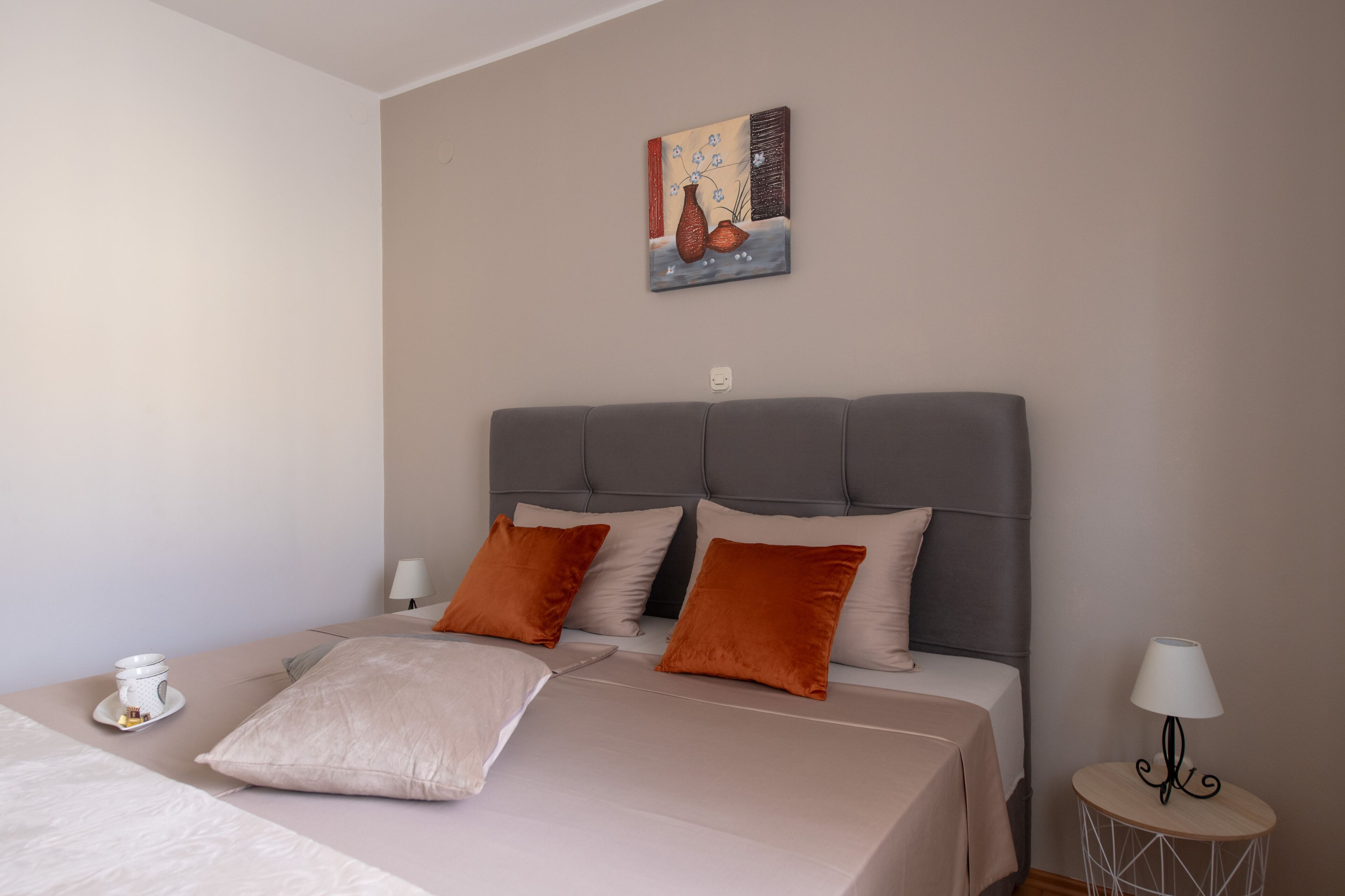 A neatly arranged bedroom with a large bed, two pillows, a bedside table with a lamp, and a wall-mounted painting.
