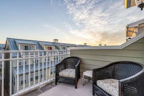 Een balkon met twee rieten stoelen en een kleine tafel, met uitzicht op naburige gebouwen en een heldere lucht.
