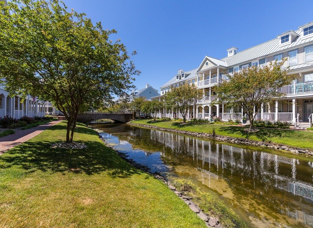 A residential area with a narrow water channel, white houses with balconies, and a tree-lined pathway.
