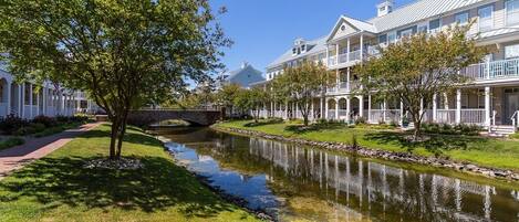 A residential area with a narrow water channel, white houses with balconies, and a tree-lined pathway.