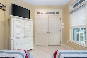 Een slaapkamer met een witte dressoir, een televisie erboven en een raam met uitzicht.