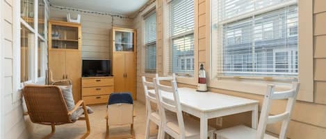 A compact kitchen with a dining area, wooden cabinets, a television, and a window with blinds.