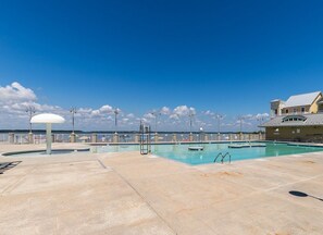 A swimming pool with a clear sky, a building with a balcony, and a fence.
