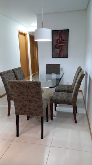 Un coin repas avec une table en verre entourée de chaises à motifs, un luminaire suspendu blanc et un tableau abstrait encadré accroché au mur.