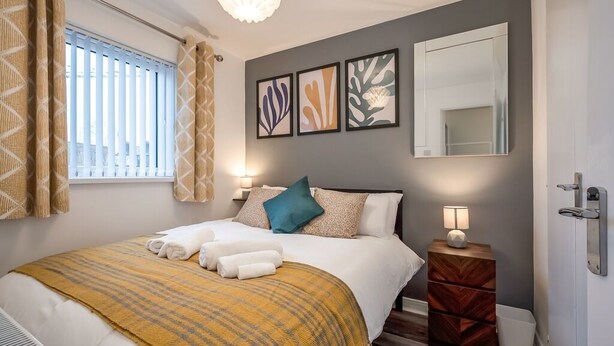 Un dormitorio ordenado con cama, lámparas de noche, mesitas de noche y una ventana con persianas.