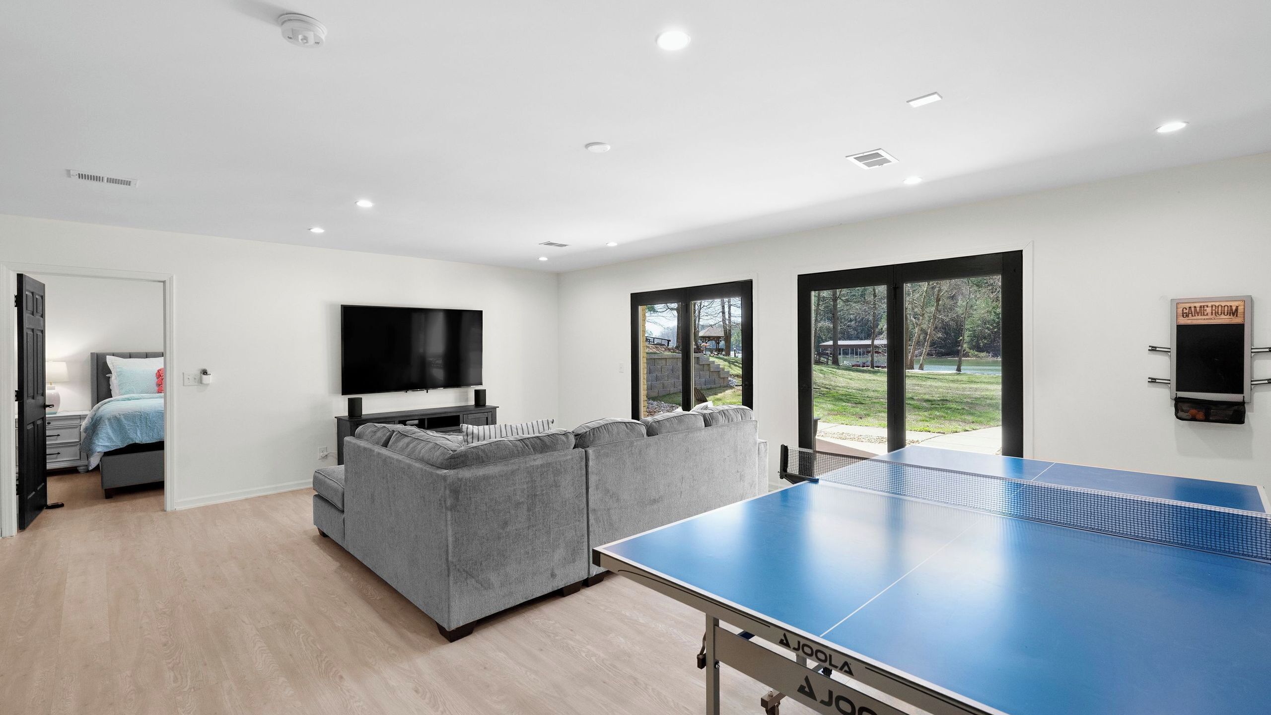 A modern living room with a large flat-screen TV, grey sectional sofa, and a ping pong table.