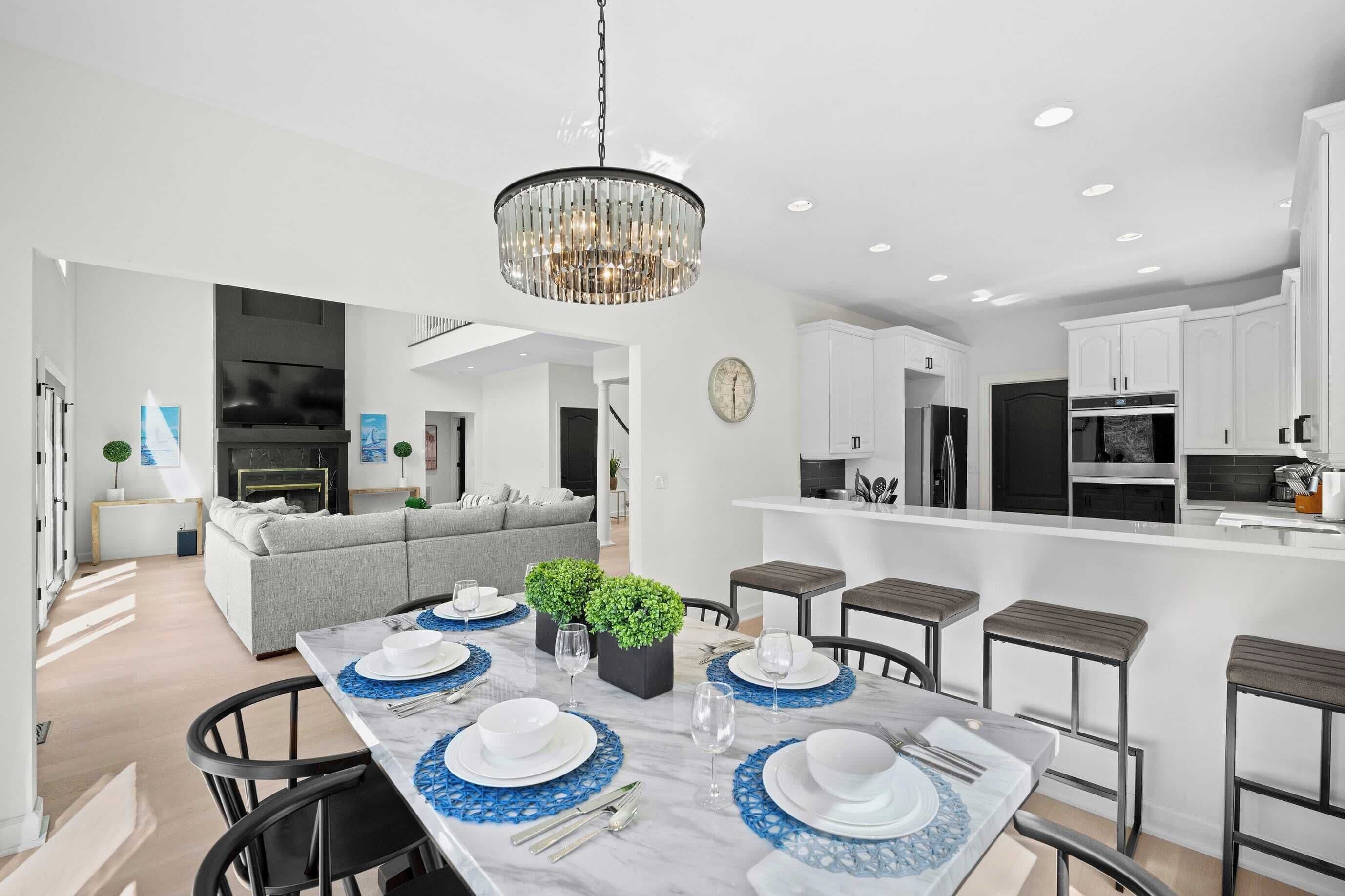 A modern kitchen with white cabinets, a central island, and a dining area with a marble table set for four.