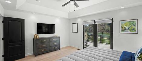 Un dormitorio con cama, ventilador de techo, televisor, cómoda y balcón con vistas.