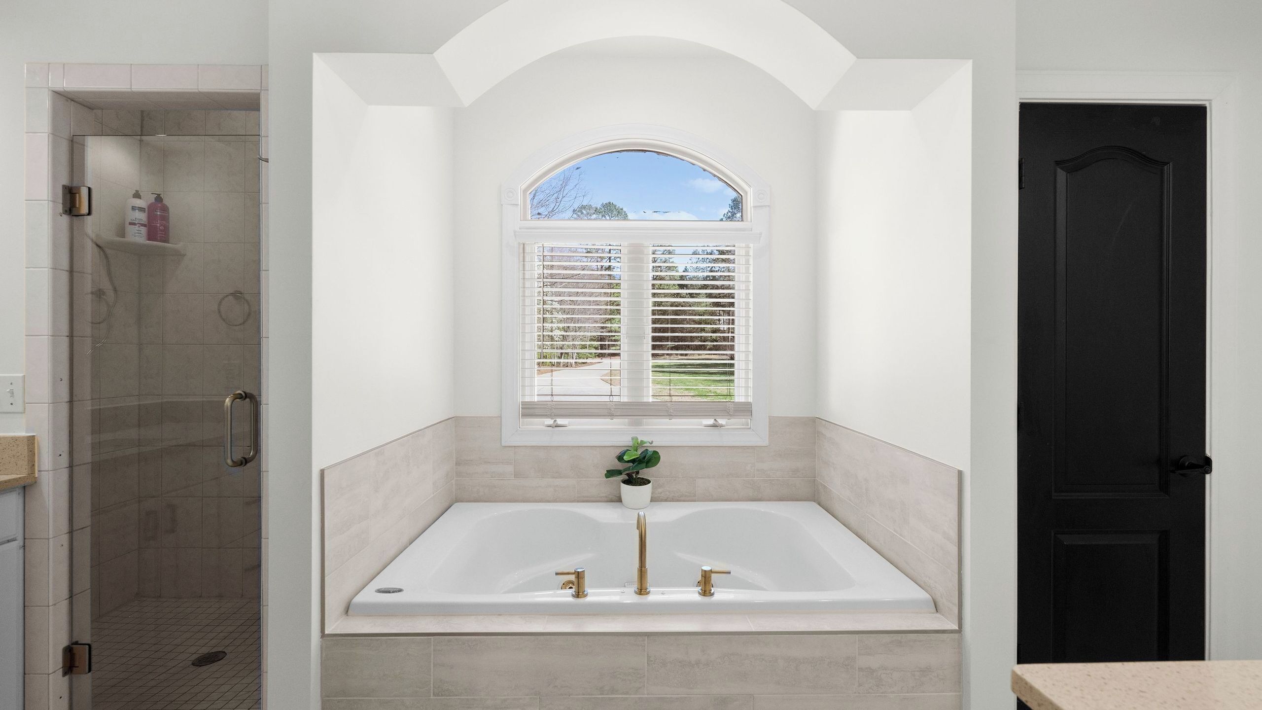 A bathroom with a bathtub, shower, and window with blinds.