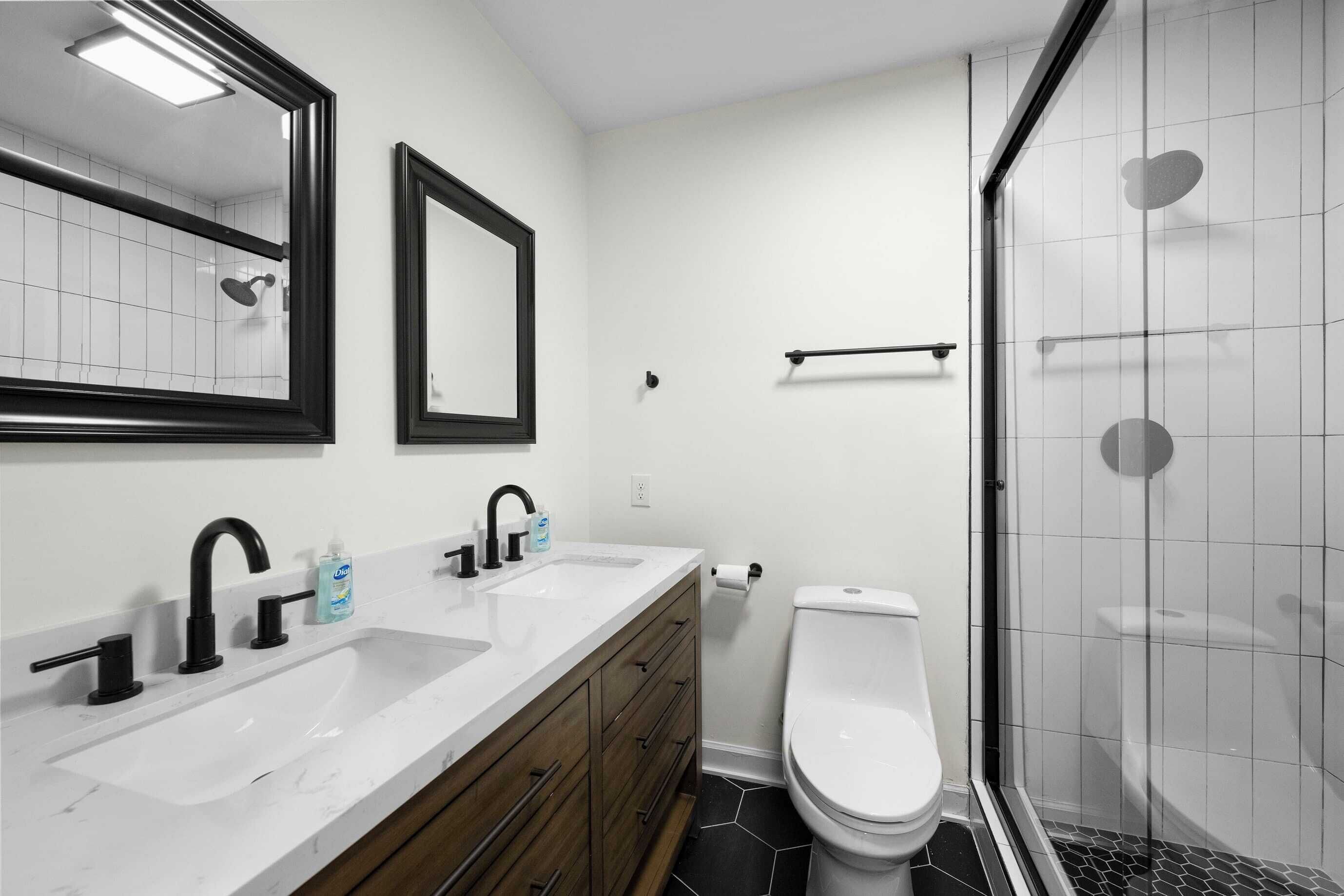 A bathroom with two sinks, a toilet, a shower, and a mirror.