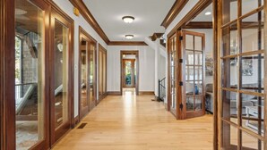 A long hallway with wooden doors and windows, a staircase, and a view of the outdoors. - Sunset Shores Resort: The Grand House by Avantstay Lakefront, Spa, Private Dock+beach, Game Room (Mooresville)