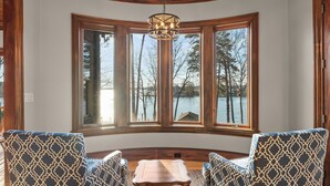 A room with a curved window, two patterned armchairs, a small table, and a hanging light fixture. - Sunset Shores Resort: The Grand House by Avantstay Lakefront, Spa, Private Dock+beach, Game Room (Mooresville)