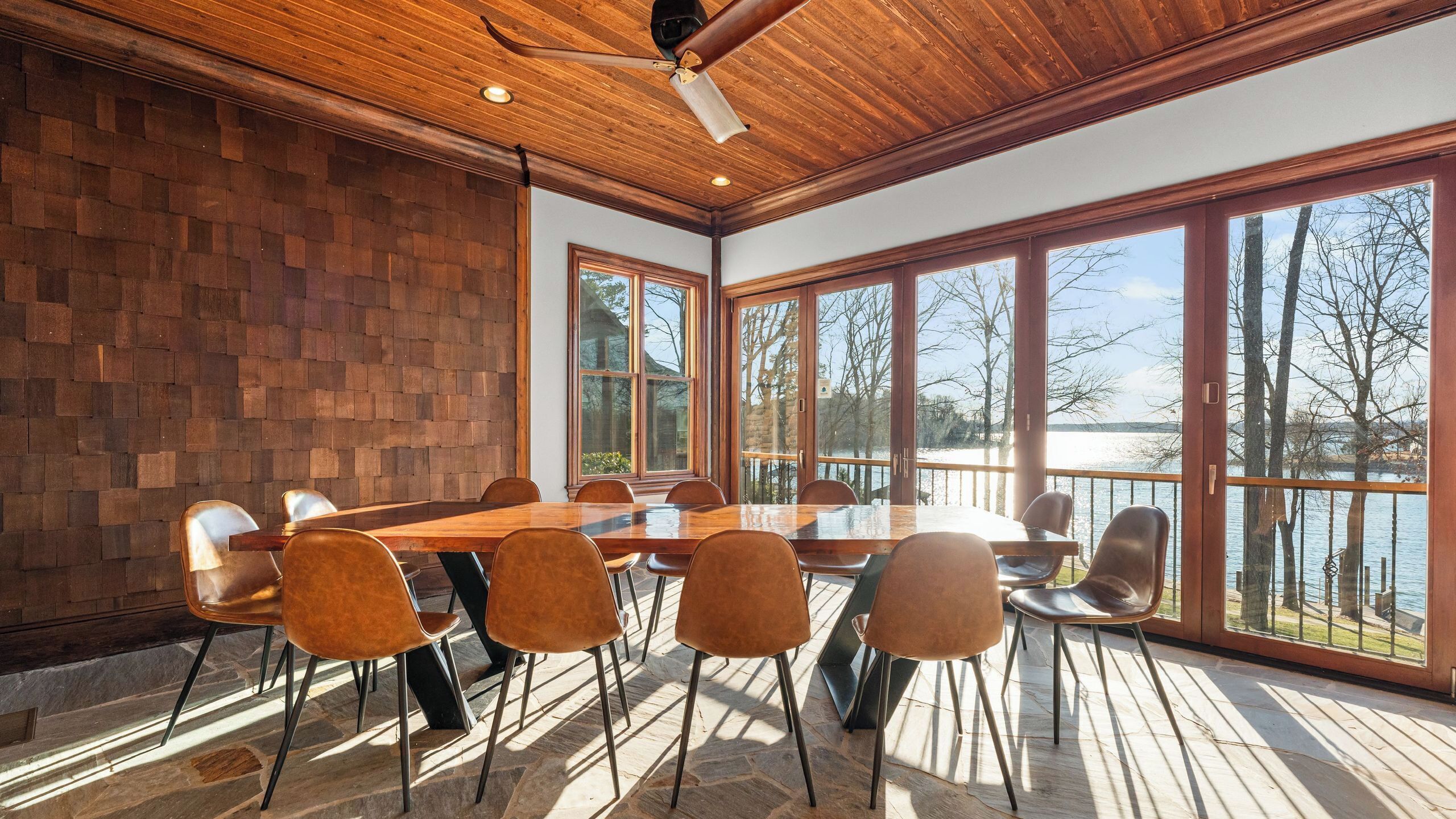 Ein geräumiger Essbereich mit Holztisch und -stühlen, großen Fenstern mit Seeblick und einem Deckenventilator.