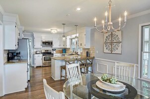 Una cocina moderna con armarios blancos, una isla central y una zona de comedor con mesa y sillas de vidrio.