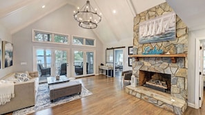 A spacious living room with a stone fireplace, large windows, and a chandelier. - A Frame of Mind by Avantstay Lakefront Retreat Hot Tub + Game Room + Dock (Sherrills Ford)