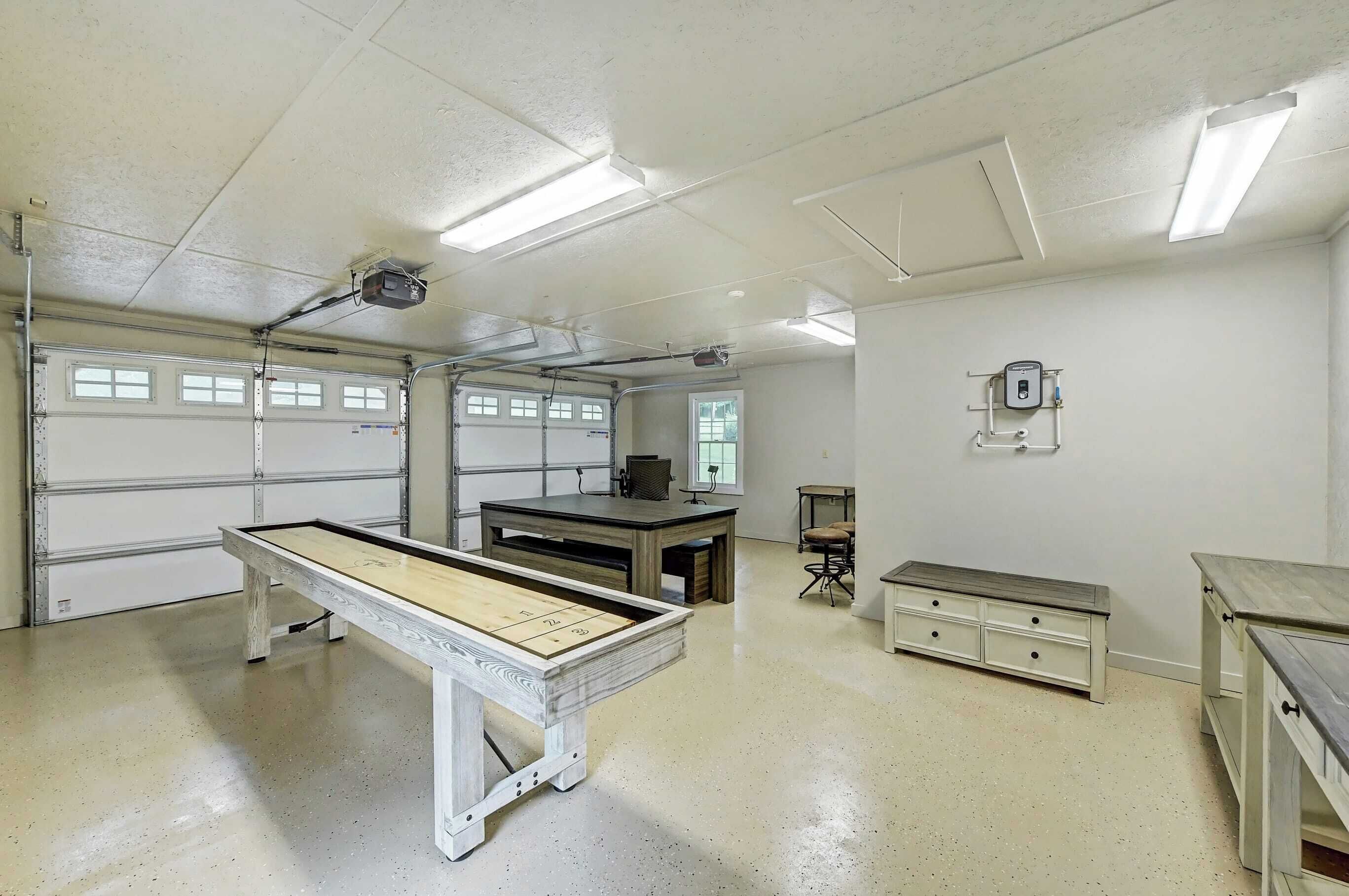 A spacious indoor area with a pool table, a desk, and a chair. There are two windows and a ceiling-mounted projector.