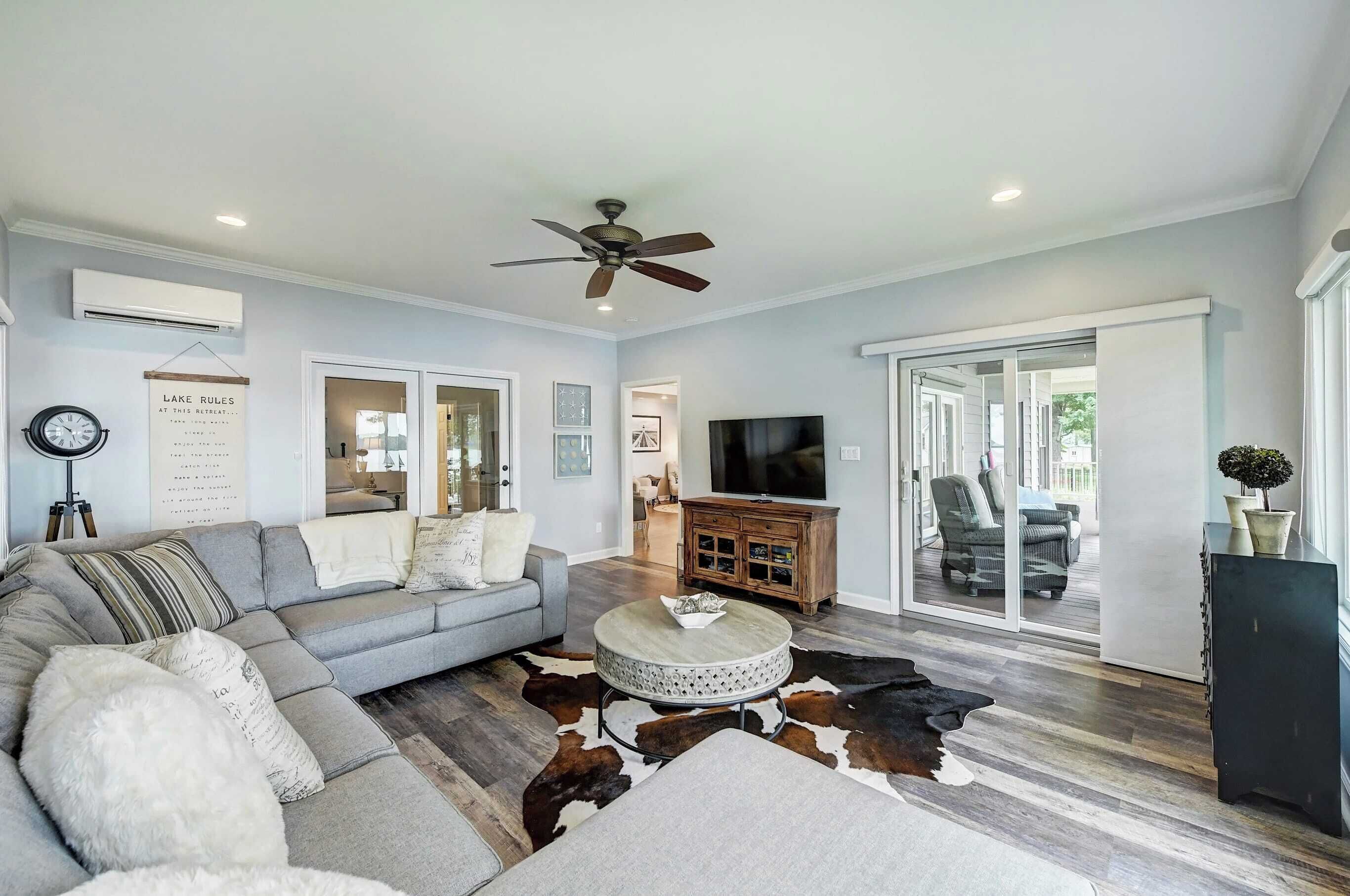 A living room with a grey sofa, a round coffee table, a ceiling fan, and a flat-screen TV.