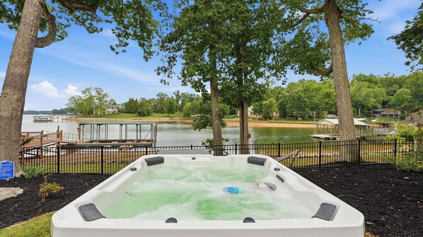 Un jacuzzi con vista a un lago y un muelle, rodeado de árboles y una valla.