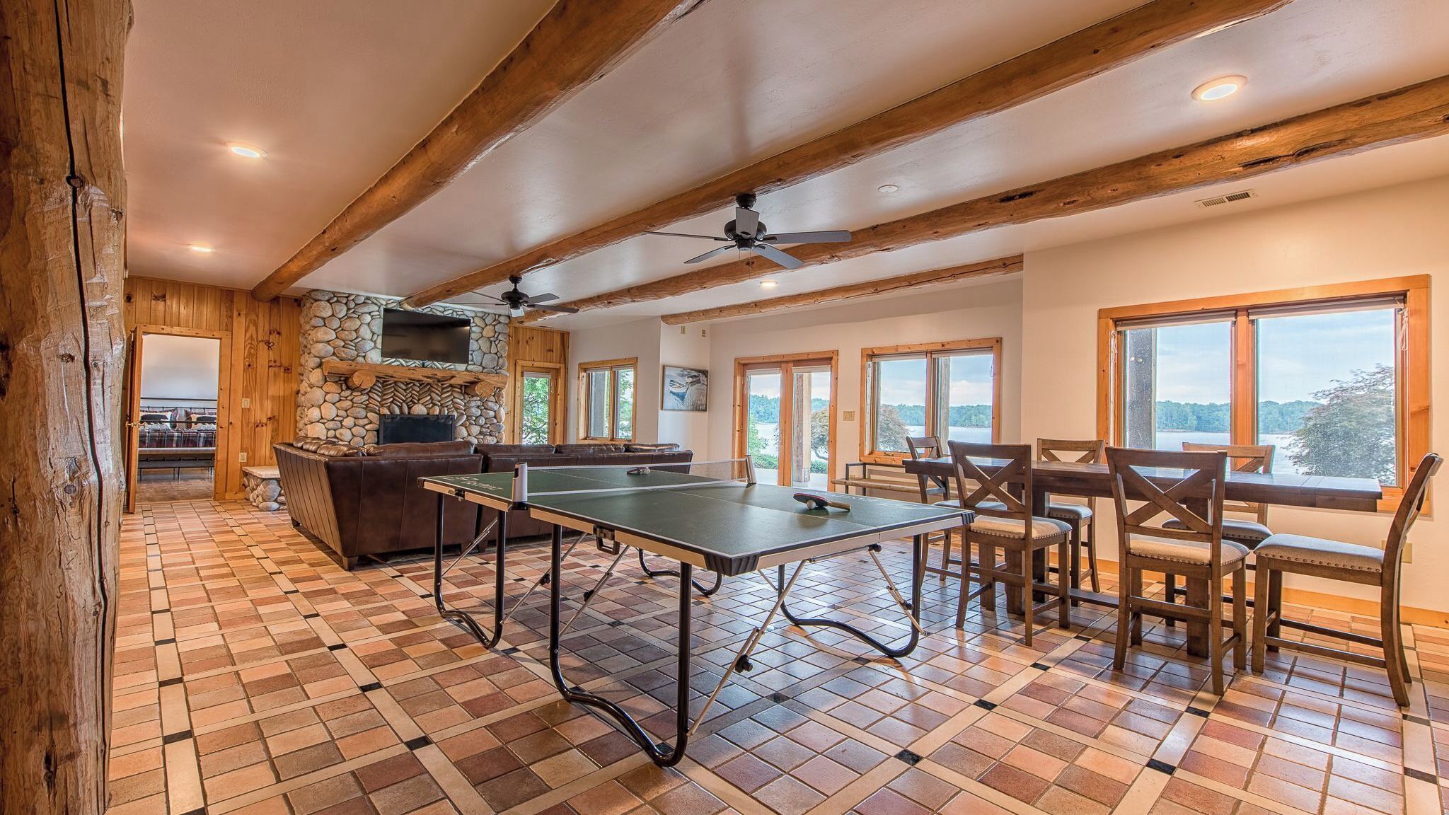 Une pièce spacieuse équipée d’une table de ping-pong, d’un coin salon, d’une cheminée en pierre et de grandes fenêtres offrant une vue panoramique.