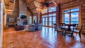 A log cabin interior with a fireplace, seating area, and large windows offering a view. - Azalea Retreat- The Lodge by Avantstay Best View (Sherrills Ford)