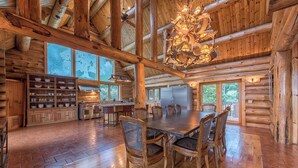 A spacious wooden dining area with a large table and chairs, a chandelier, and a kitchen with wooden cabinets and a refrigerator. - Azalea Retreat- The Lodge by Avantstay Best View (Sherrills Ford)